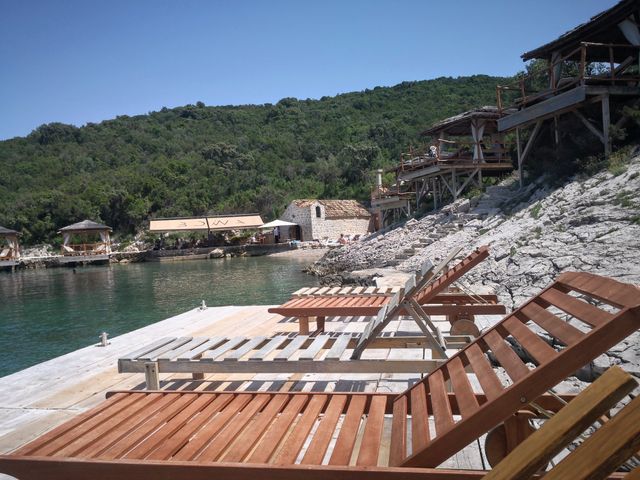 Tranquil bay with wooden lounge chairs on rocky shore, overlooking crystal-clear waters and lush green hillside in Elafiti Islands