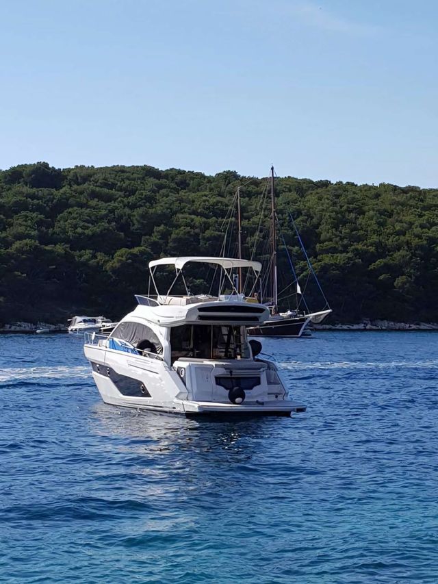 A sleek, white Cranchi yacht sits anchored near a lush green island, ready for a luxury charter experience in Dubrovnik.