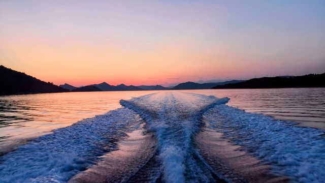 Sunset view from a boat, showing wake trails on calm water surrounded by silhouetted Elaphite islands.