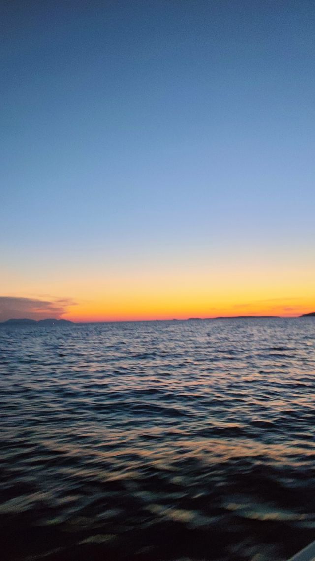 Serene sunset over calm sea with distant islands silhouetted against colorful sky gradient