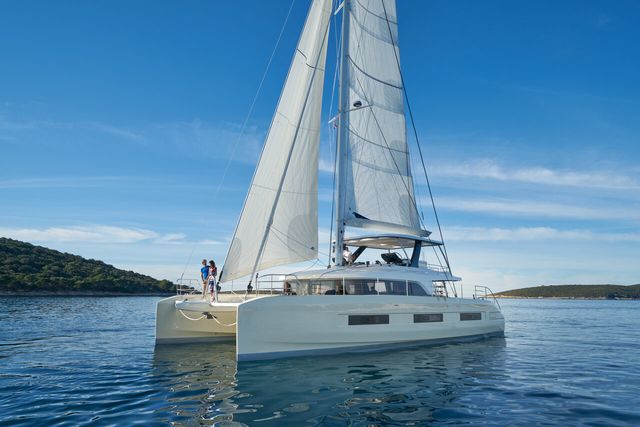 Luxury Lagoon Sixty 5 Amada Mia catamaran sailing in Croatia's crystal-clear waters under a blue sky, with a couple on deck.