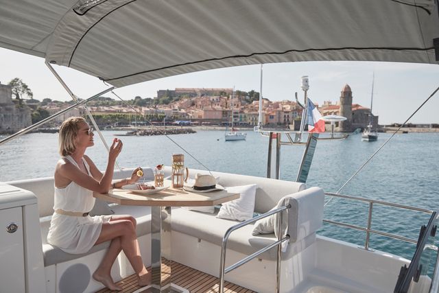 A woman relaxes on the flybridge of a luxury yacht, enjoying drinks and fruit while overlooking a charming Mediterranean coastal town in France.