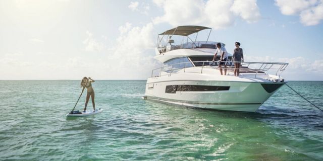 Prestige 420 luxury yacht anchored in Croatia's Adriatic Sea. A woman paddleboards while guests relax on the flybridge.