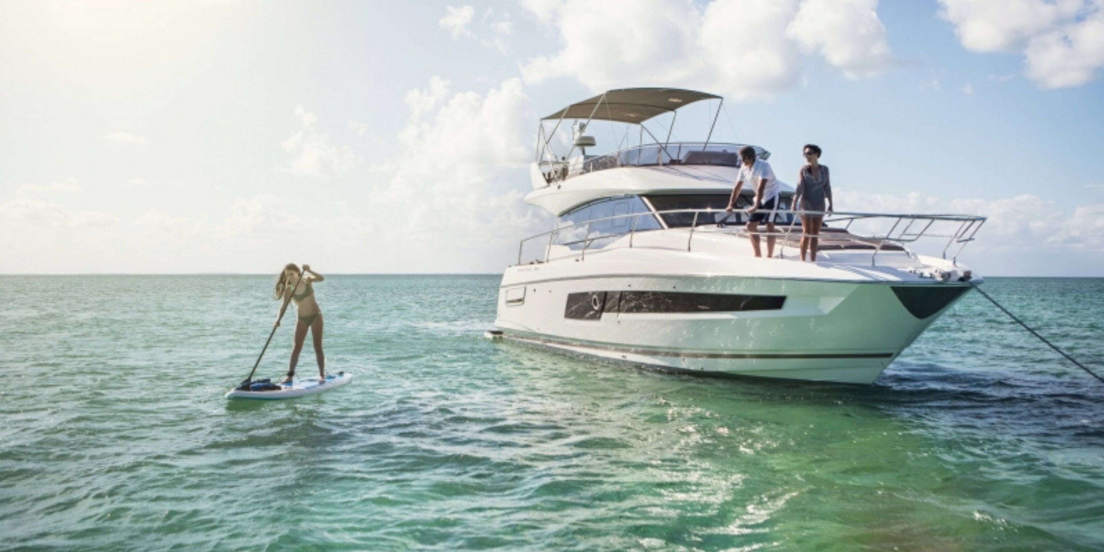 Prestige 420 luxury yacht anchored in Croatia's Adriatic Sea. A woman paddleboards while guests relax on the flybridge.